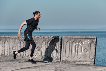 Side view of Healthy Handsome Active Male running on sidewalk in morning At Sea. Health conscious concept with copy space.