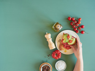 Obraz na płótnie Canvas hand with avocado and tomato toast in a breakfast table