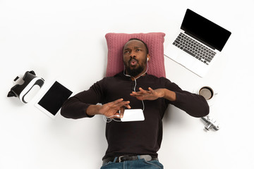 Young african-american man using devices, gadgets isolated on white studio background. Concept of modern technologies, gadgets, tech, emotions, ad. Copyspace. Gaming, shopping, meeting online