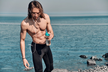 Shot of Topless Healthy Handsome Active Man With Fit Muscular Body standing outdoors holding water bottle. Fitness man taking a break after running workout.
