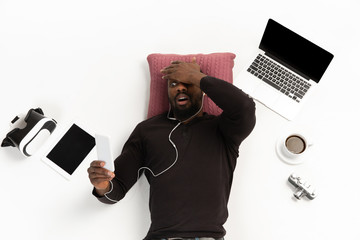 Young african-american man using devices, gadgets isolated on white studio background. Concept of...
