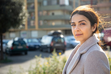 ragazza mora con la coda guarda seria , sullo sfondo palazzi e auto parcheggiate