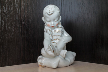 SCULPTURE PORCELAIN STATUETTE. THE BOY IS SITTING ON A PILLOW