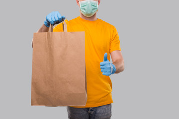 Delivery Man Wearing Medical Mask and Gloves With Paper Bag in Hands. Yellow Tshirt Delivery Boy. Home Food Delivery.