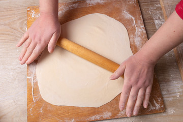 Female hands rolling dough on a cutting board with a rolling pin. Cooking at home.