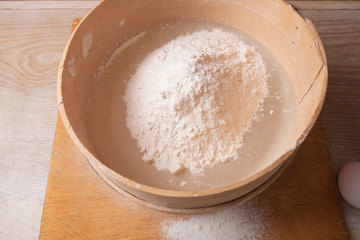 Large bowl, cutting board, sieve for sifting flour on the table. Female hands sifting flour in the home kitchen.
