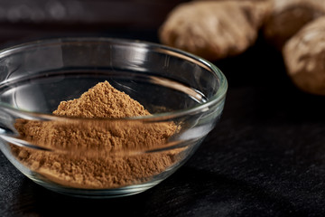 Ground ginger in a plate on a black background. In the background, the root of ginger. side view. sharp powder. macro photo. Against viruses and diseases.