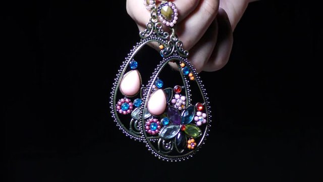 A woman shows two gem studded jewellery earrings in the fingers.