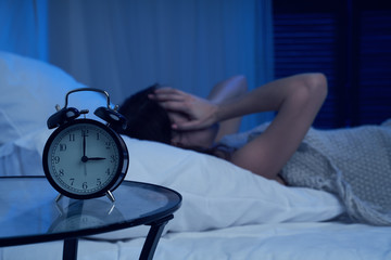 Unhappy woman with insomnia lying on bed next to alarm clock at night - obrazy, fototapety, plakaty
