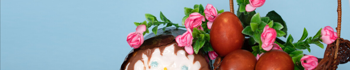 Easter cake, red chicken eggs in a basket and flowers on a blue background: happy Easter