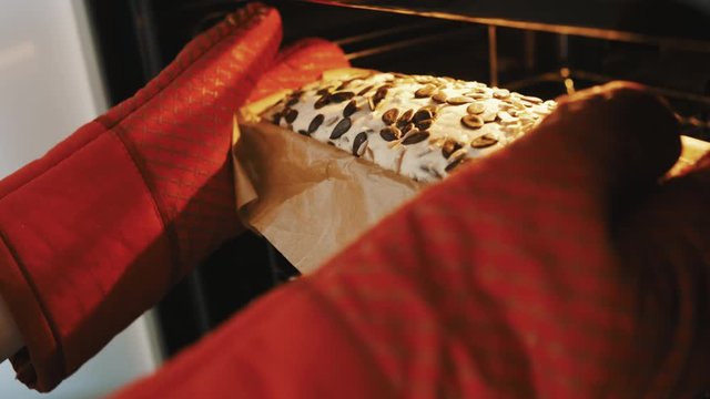 Person with red kitchen gloves putting homemade bread with pumpkin seed in the oven. Close up slow motion shot