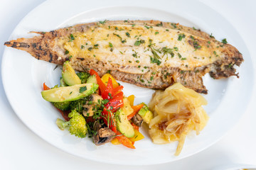 Sole meunière fish with grilled vegetables and caramelized onions on a white plate with white background. LENGUADO MENIER