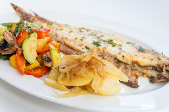 Sole meunière fish with grilled vegetables and caramelized onions on a white plate with white background. LENGUADO MENIER