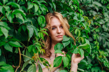 Portrait of a young beautiful woman, hiding in of wild grape leaves.