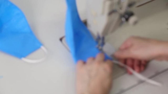 Phased sewing of medical masks from blue fabric on a sewing machine. Close up industrial sewing machine makes a seam. The concept of deficiency of medical masks during the coronavirus pandemic.