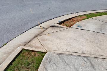 Asphalt street and concrete sidewalk with graded ramp between, green grass, horizontal aspect