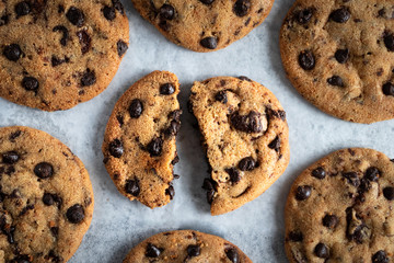 flat lay of chocolate chip cookies with the middle one broken on a light grey backdrop