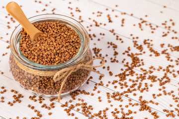 Close-up of buckwheat in a glass jar with a wooden spoon, jute cord and scattered on a white wooden table.