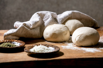 Dough for italian pizza napolitana cooking. Three balls of fresh homemade wheat dough and ingredients in ceramic plates above on wooden kitchen table. Home baking.