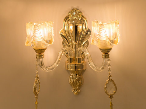 Image of a wall chandelier with amber glass plafonds mounted on transparent fittings and a gold stand. The concept of classic decor in the room. Close up. Soft warm filter, selective focus.
