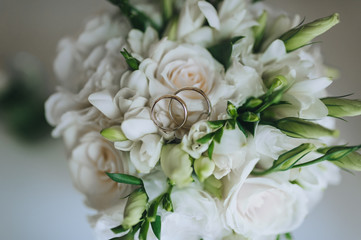 Wedding gold rings close-up on a bouquet of fresh white flowers: roses, eustomas. Photography, concept.