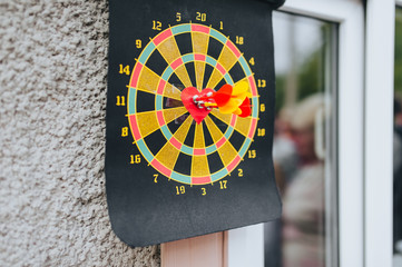 Darts sticking out in the center of a round dart board with a red heart on a black canvas. Wedding...