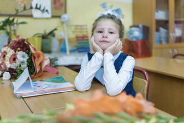 A small schoolgirl of primary classes sits at a desk and listens to a lesson. Day of knowledge. First of September. The beginning of the school year. Concept of education.