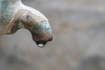 Water that is dripping from the vintage old brass faucet with blurred cement wall background close-up.