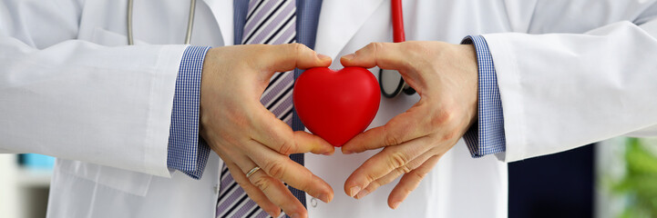Fototapeta premium Male medicine doctor hands holding and covering red toy heart