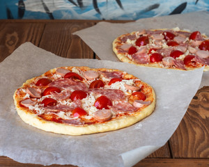 Two blanks for pizza with sausage and tomatoes at home on a wooden table