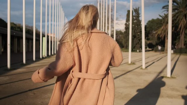 Conceptual shot of beautiful blond girl in coat running away through the park