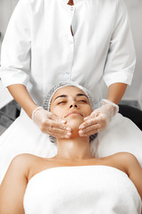 Naklejka premium Cosmetologist applying cream on female face in cosmetology salon.