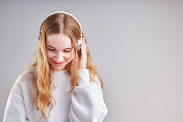 Young woman girl listening to music streaming content having fun watching video enjoying video chat talking with friends making gestures faces using smartphone earphones headphones