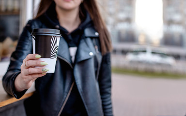 the girl holds and hands out a hot cappuccino in a White paper Cup. We buy coffee at a coffee shop. The concept of buying