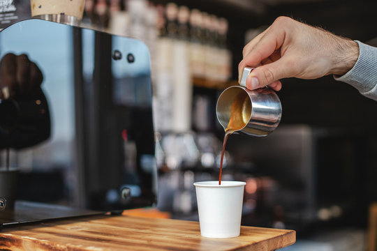 Close-up image of male hands pouring milk and preparing fresh cappuccino, coffee artist and cooking concept, morning coffee.