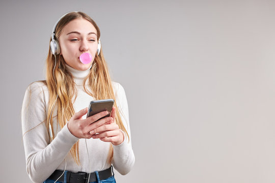 Young woman girl listening to music streaming content having fun watching video enjoying video chat talking with friends making gestures faces using smartphone earphones headphones