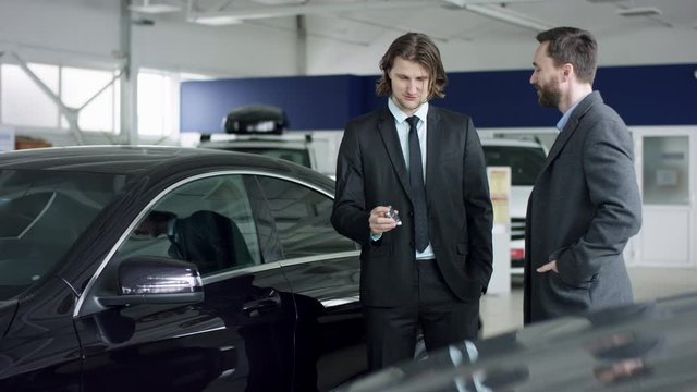 Broad overview of salesman shaking hands with male customer, car dealer gives key to client and then they shake hands in dealership showroom