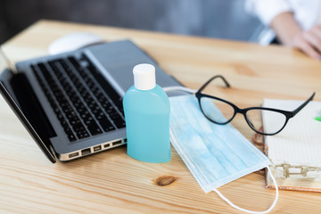 Medical protective mask and hand sanitizer in a bottle, laptop pen glasses notebook lies on a wooden table