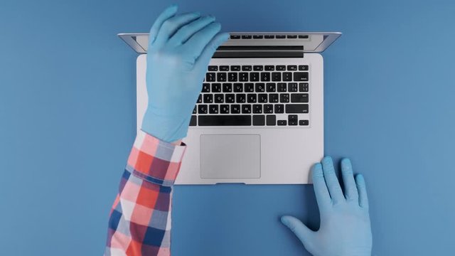 Male hands in protective gloves moving a laptop on a blue background. Top view, studio shooting