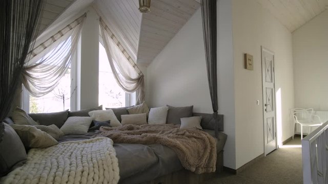 Interior of a modern house spacious hallway with big soft resting place. Contemporary wide sofa with many pillows and light window onder wooden loft ceiling.