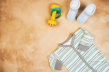 Clothes and baby goods. Bodysuit for infant boy, baby booties, rattle. Top view, copy space.