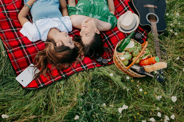 Fototapeta na wymiar Two cheerful young fashionable women lying down on the picnic blanket and relaxing.