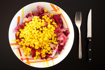 Salad with corn on black table, top view