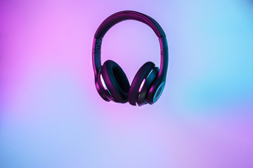 Retro 90s style photo of black stylish wireless headphone in neon lights.