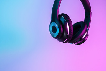 Retro 90s style photo of black stylish wireless headphone in neon lights.