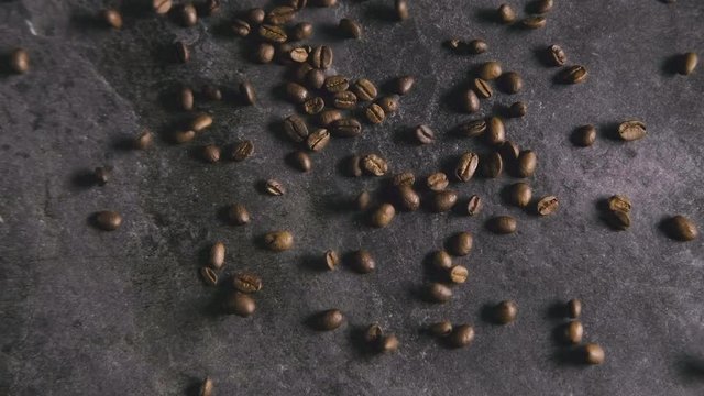 Close-up of coffee beans being tossed into frame on a grey granite background.