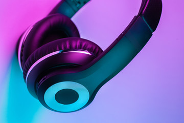 Retro 90s style photo of black stylish wireless headphone in neon lights.