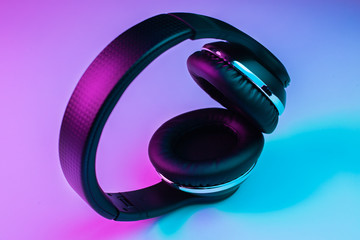 Retro 90s style photo of black stylish wireless headphone in neon lights.