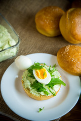 Homemade bun with cheese spread, fresh arugula and boiled egg in a plate
