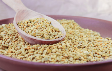 Yellow bee pollen in a brown ceramic plate and in a wooden spoon
